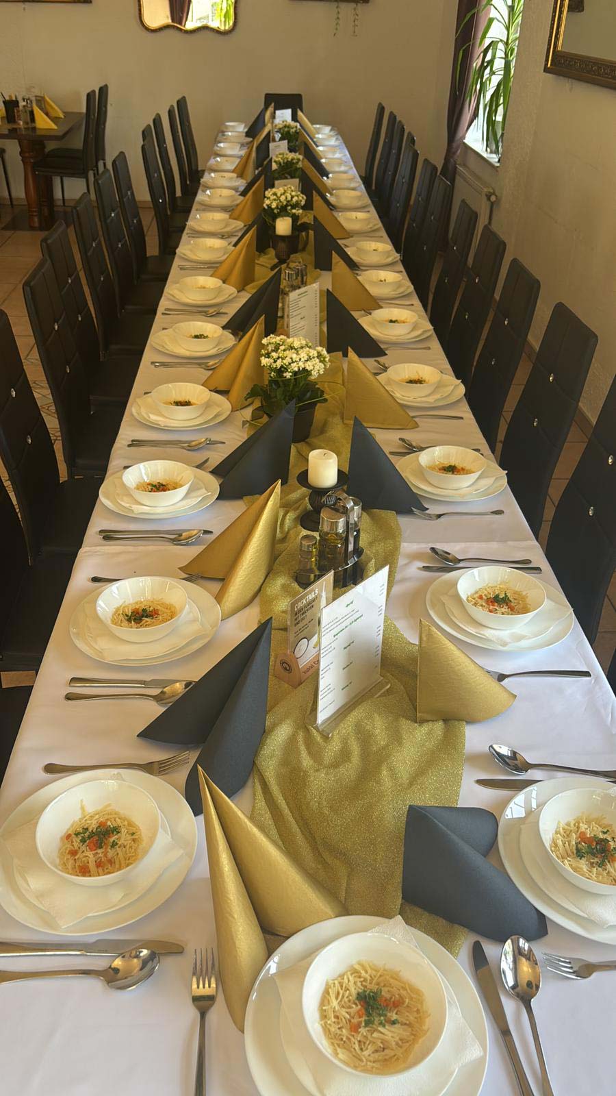 Eine festlich gedeckte Tafel mit schwarzen Stühlen und Suppentellern auf weißem Tischtuch