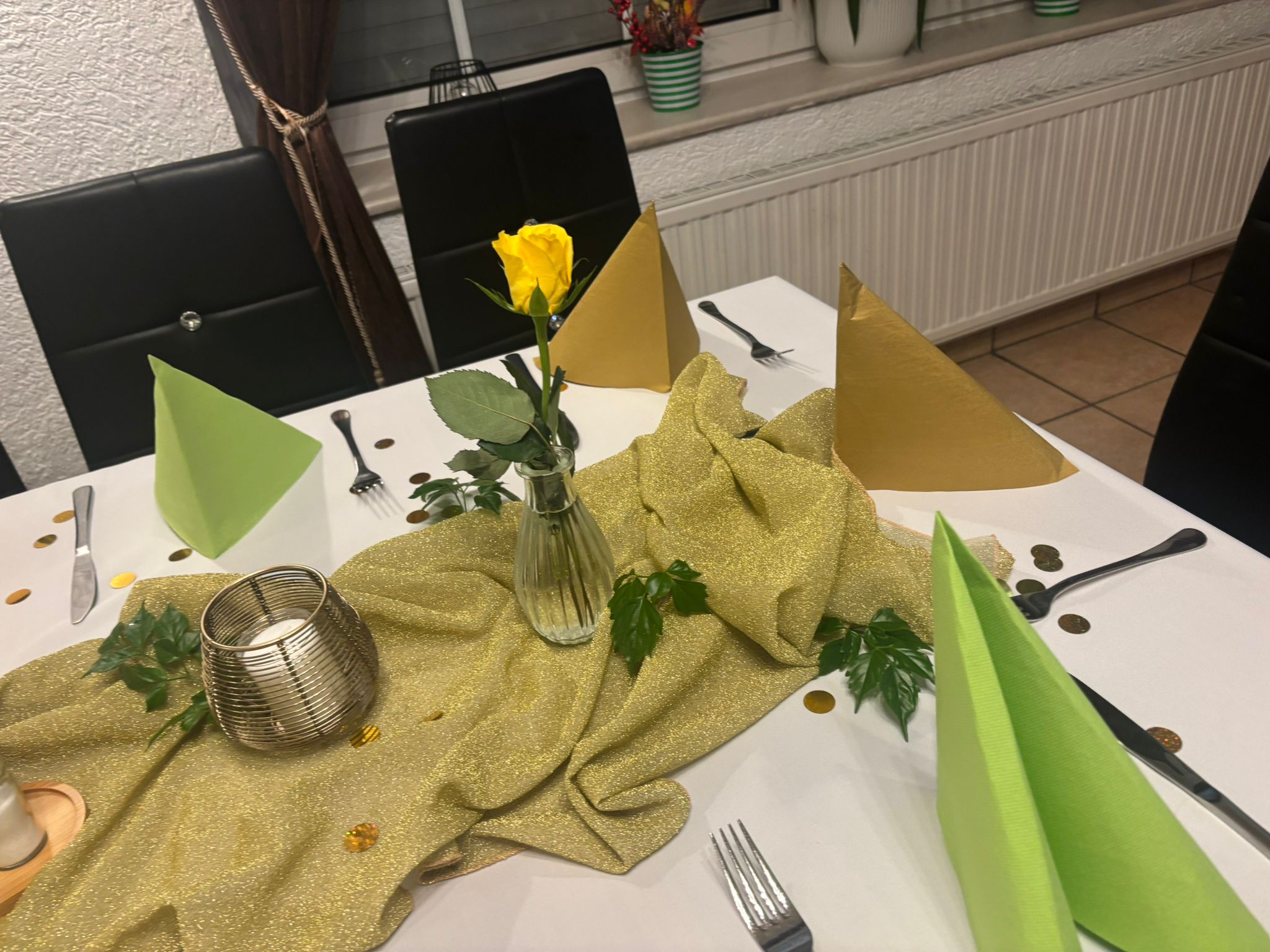 Festlich gedeckter Tisch mit gelber Rose, grün goldenen Servietten und Deko