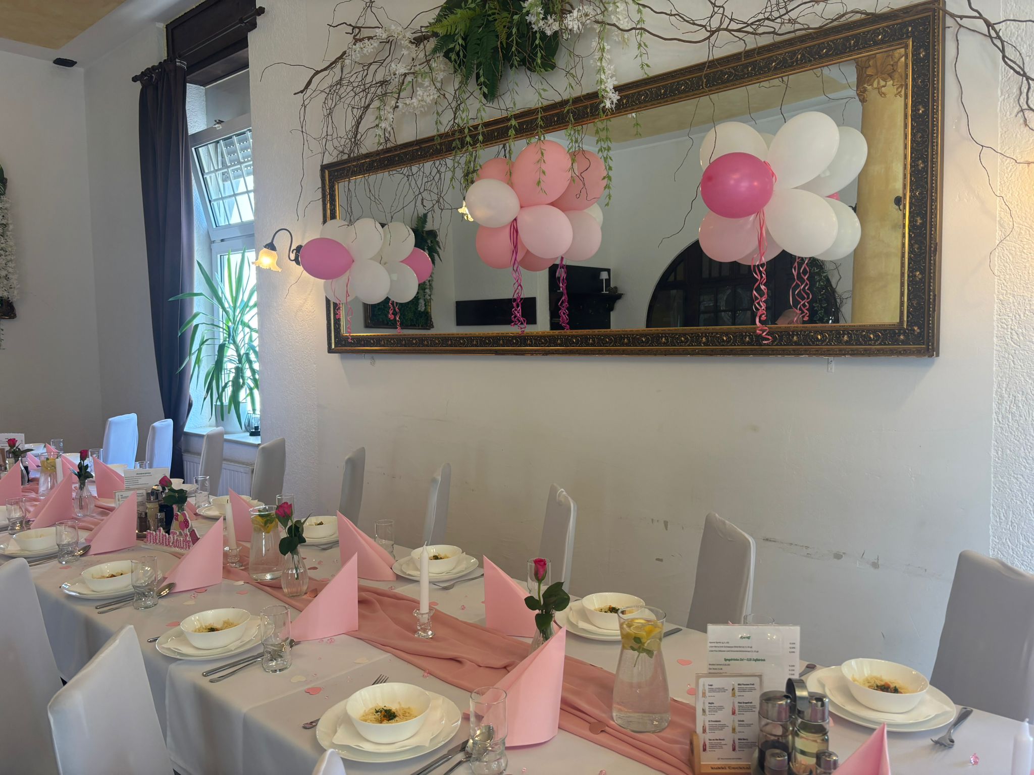 Festlich gedeckter Tisch mit rosa Servietten, weißen Stühlen und Ballondeko in Pink
