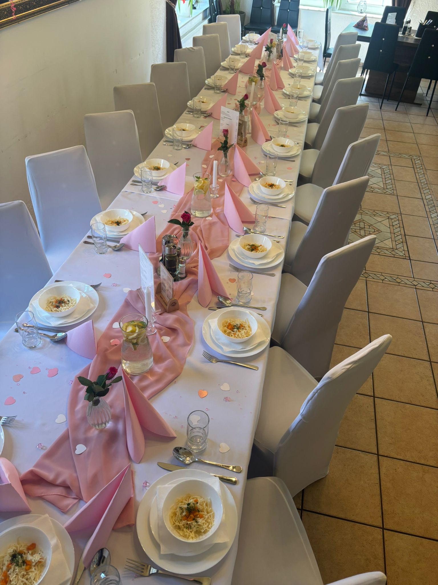 Festlich gedeckter Tisch mit weißen Stühlen und rosa Dekoration für ein besonderes Event