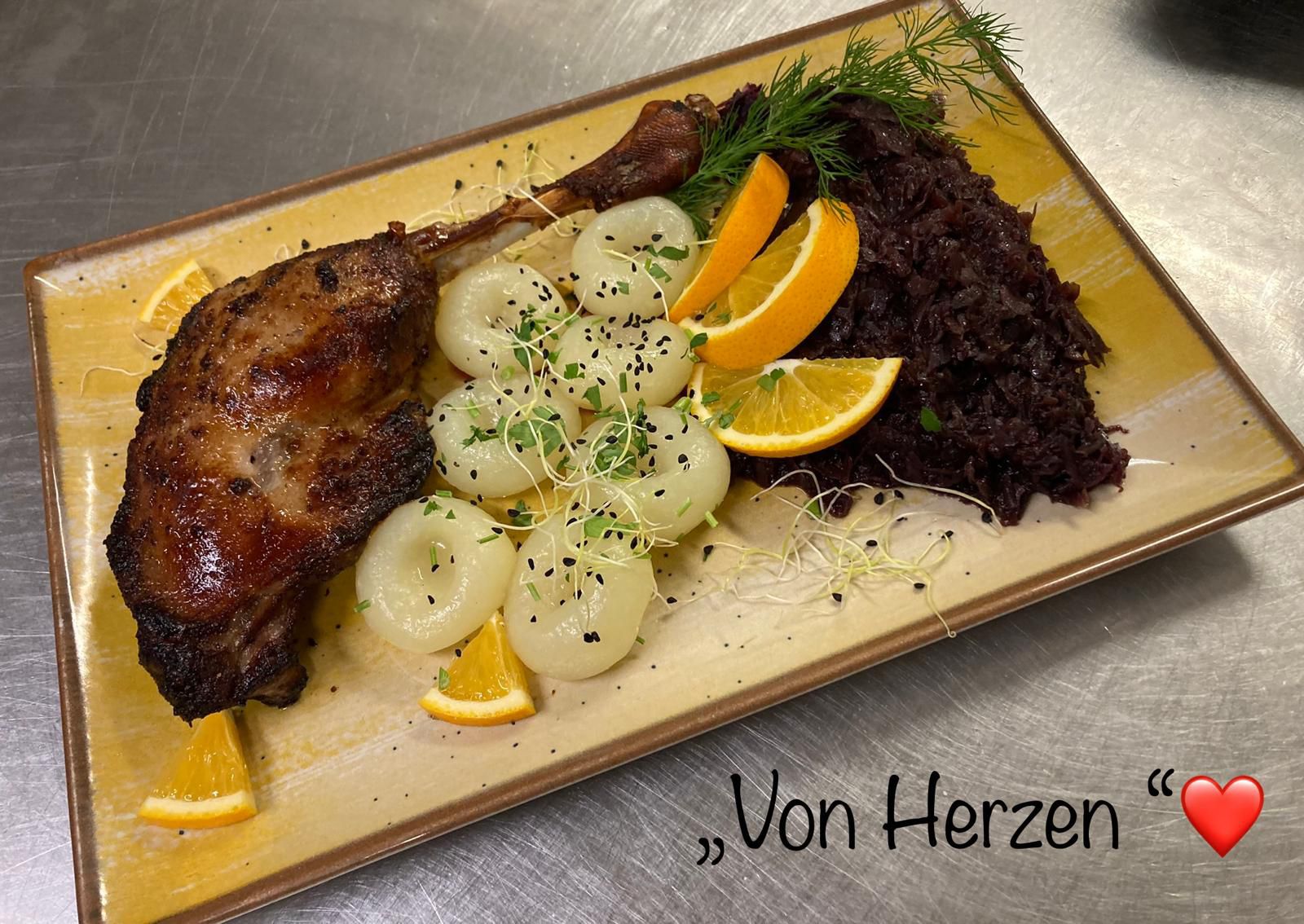 Knusprige Gänsekeule mit Salzkartoffeln, Rotkohl, Orangenscheiben und frischen Kräutern